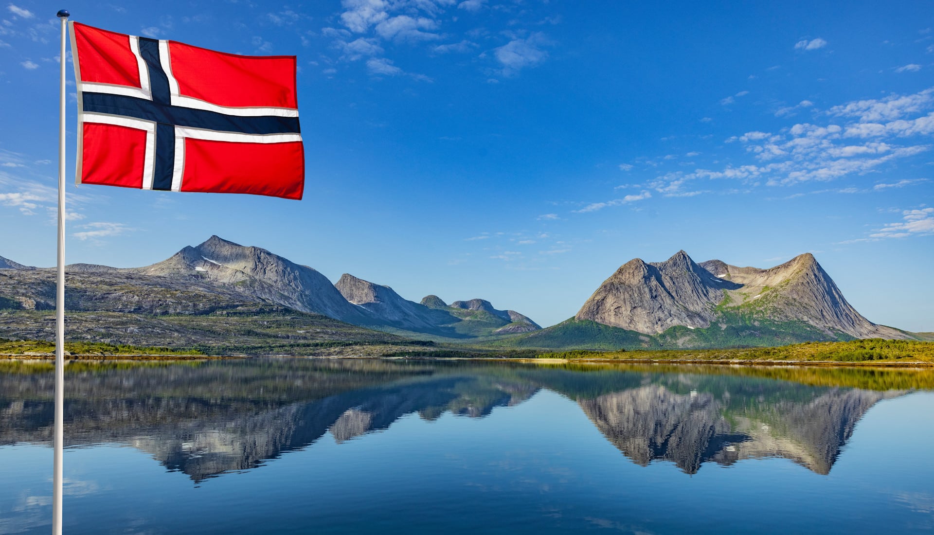 Norwegische Flagge vor in einem See spiegelnden Bergen der Ofoten